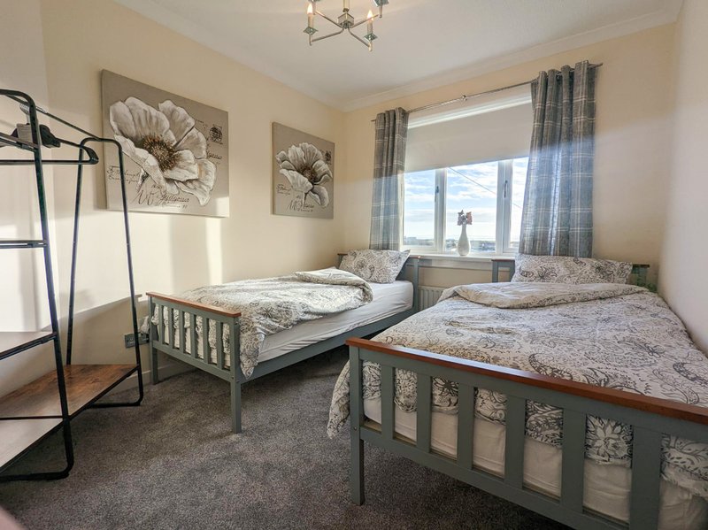 Twin bedroom with two single beds, floral wall art, window with grey curtains and clothes rail