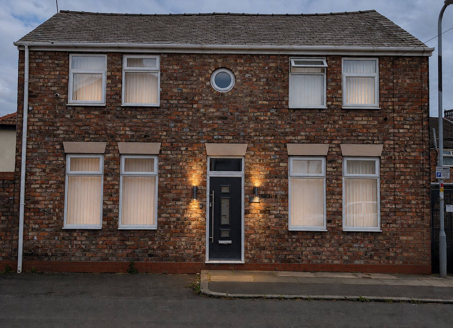 Two-storey brick house with black door, white-framed windows and uplit facade