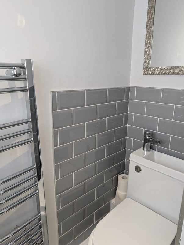 Modern bathroom with gray subway tile, white toilet, heated towel rail and mirror