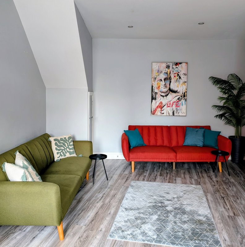Modern living room with red and green sofas, blue cushions, artwork, and potted plant