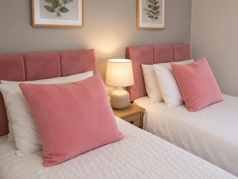 Twin bedroom with pink upholstered headboards, white bedding, pink cushions and botanical wall art