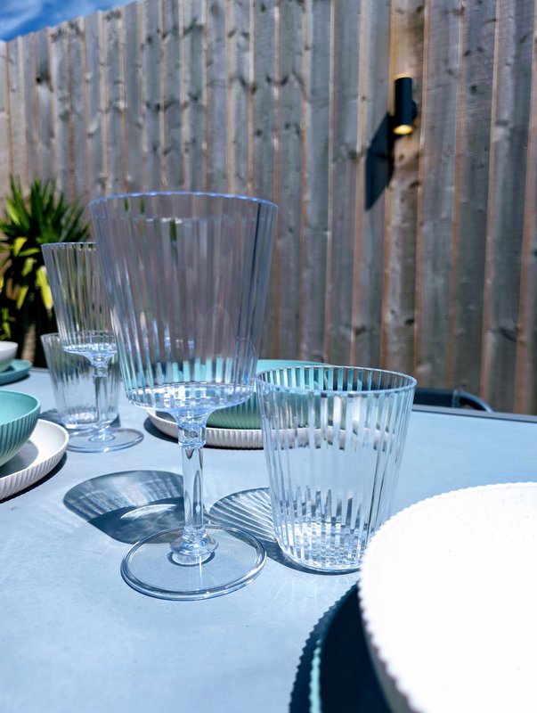 Outdoor dining table with glassware and place settings, weathered wooden fence backdrop