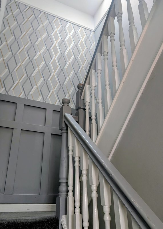 Staircase with white spindles, metal handrail, and patterned ceiling skylight