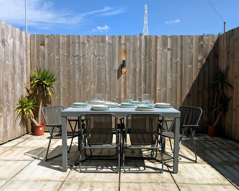 Outdoor patio with dining table, chairs, potted plants and wooden fence