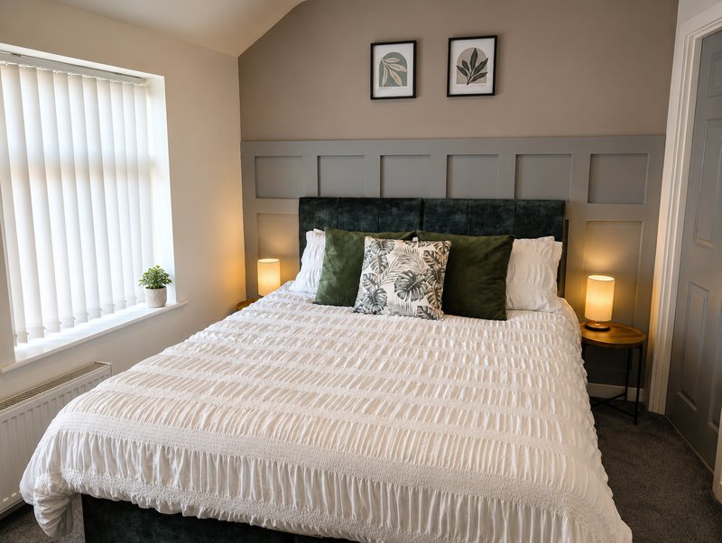 Modern bedroom with double bed, green and cream pillows, bedside lamps, and framed wall art