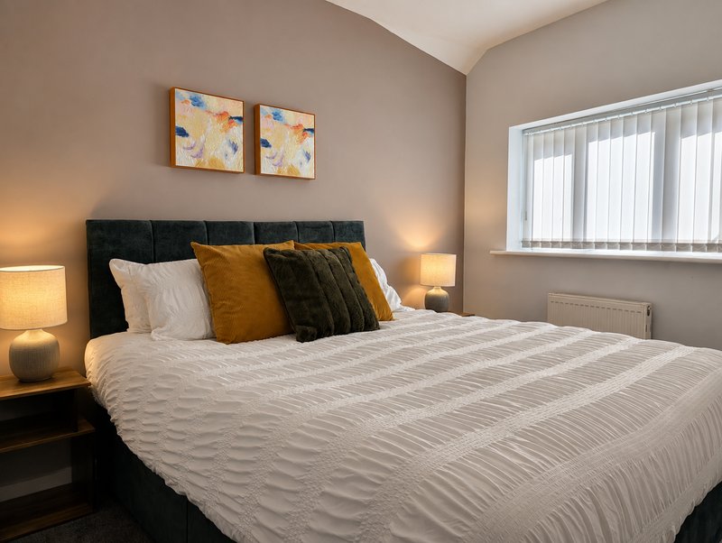Modern bedroom with black upholstered bed, white bedding, gold and black cushions, bedside lamps and artwork