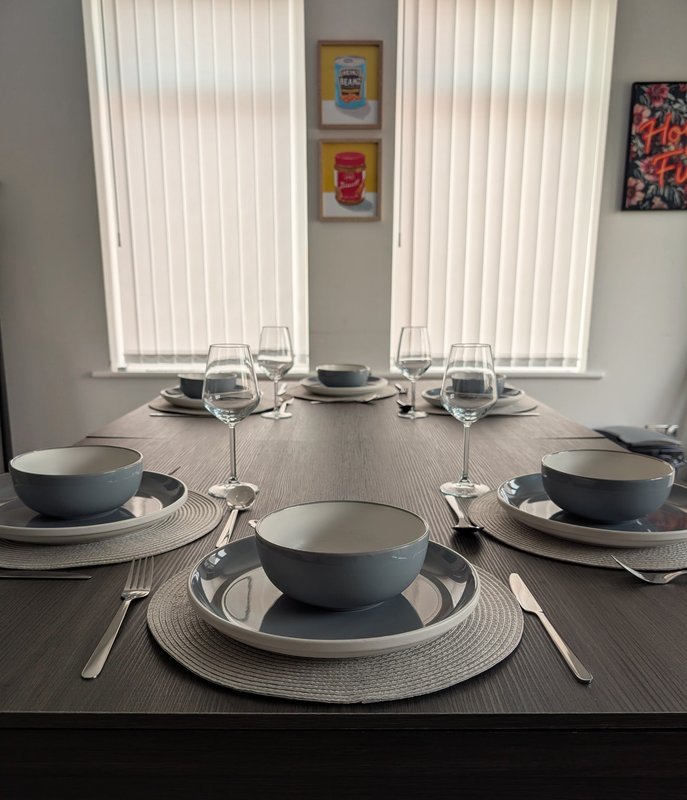 Dining table set for three with place settings, glasses, and bowls near windows