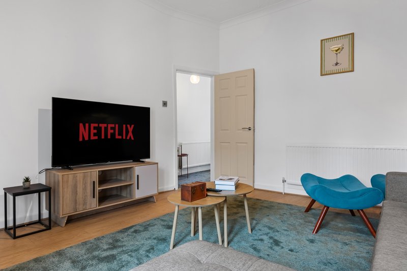Living room with TV on wooden stand, wooden coffee table, blue armchair, and beige door