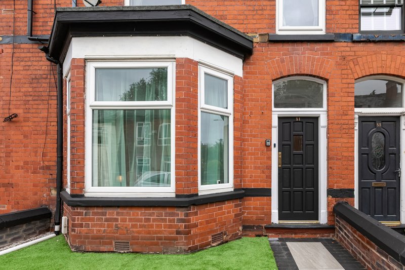 Red brick terraced house exterior with bay window, black doors and green front garden