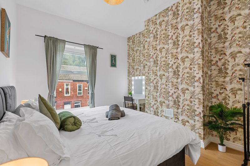 Bright bedroom with double bed, floral wallpaper feature wall, window view of red brick building