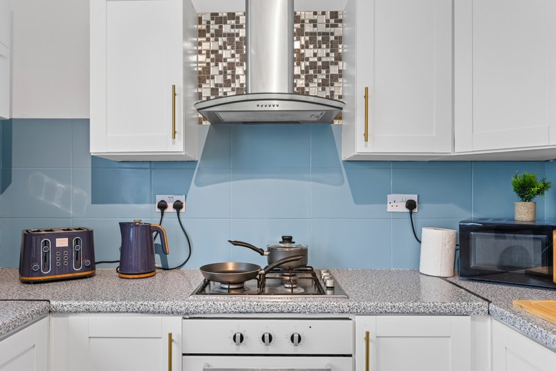 Modern kitchen with white cabinets, blue tile backsplash, gas stove and extractor hood
