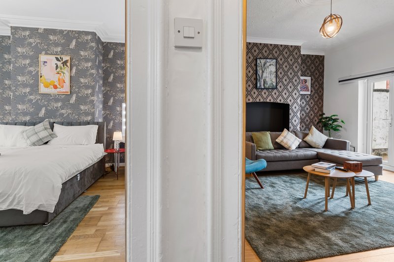 Open-plan bedroom and living room with patterned wallpaper, wooden furniture, and blue rug