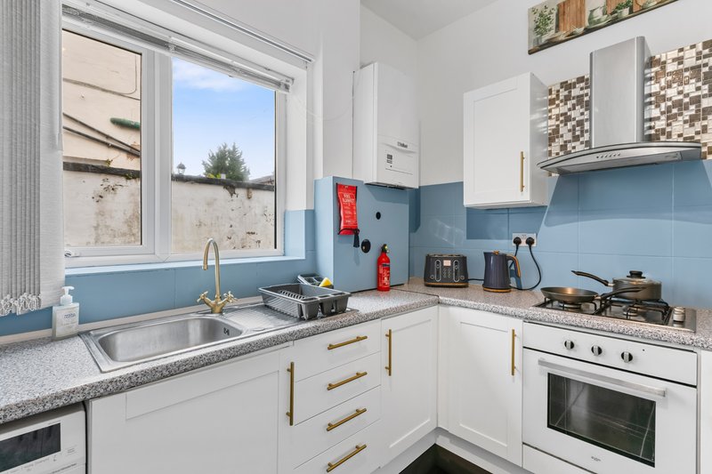Modern kitchen with white cabinetry, blue splashback tiles, granite countertop and window view