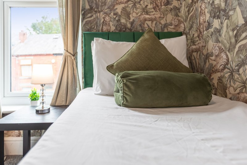 Bedroom with double bed, green headboard, patterned wallpaper and window view