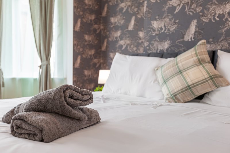 Bedroom with white bedding, folded towel, plaid cushion and patterned headboard