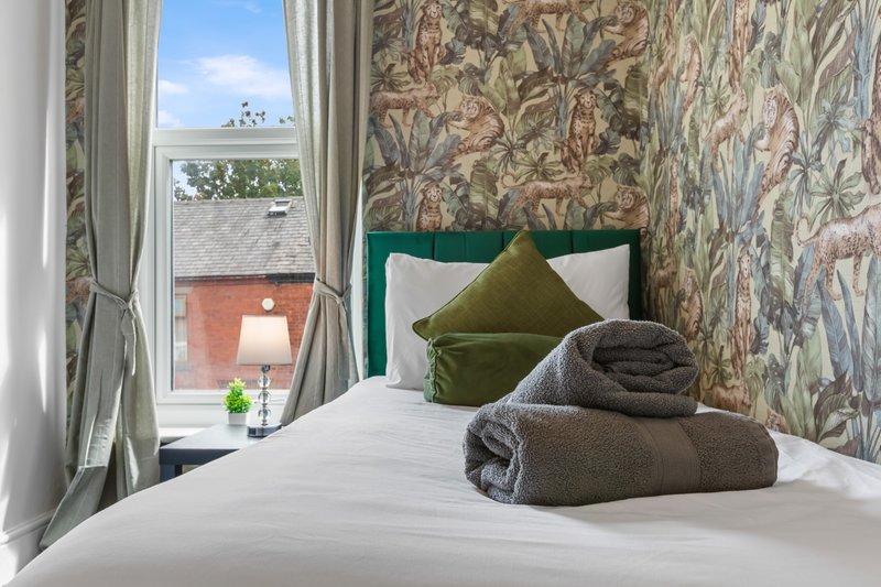 Bedroom with double bed, green headboard, patterned wallpaper, window with curtains and exterior view