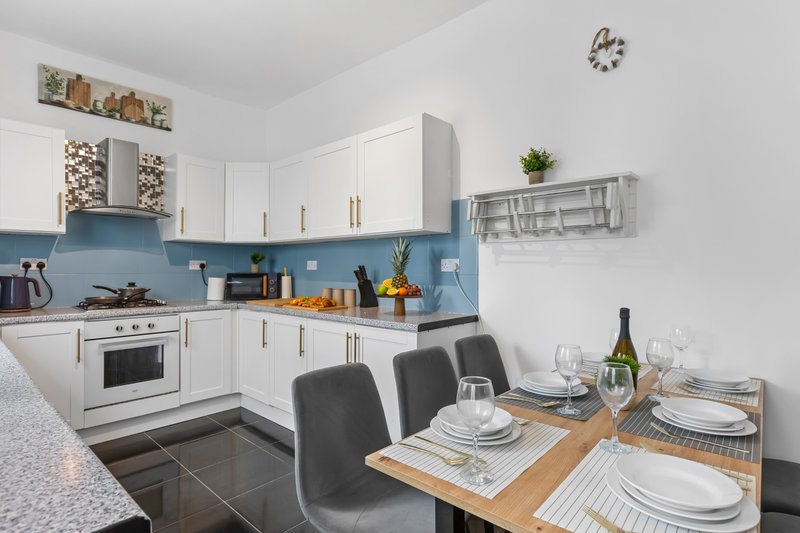 Modern kitchen with blue backsplash, white cabinetry, and wooden dining table set for two