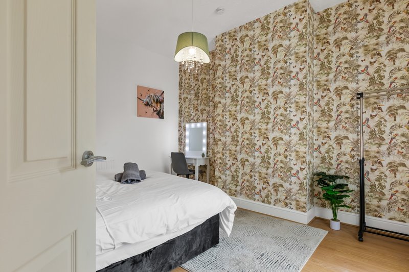Bedroom with double bed, floral wallpaper, pendant light, and wooden flooring