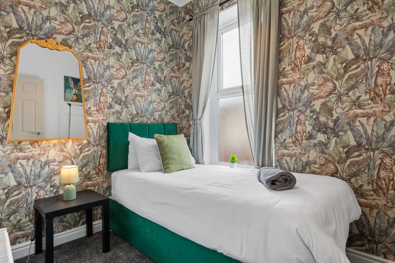 Bedroom with patterned wallpaper, double bed with green headboard, bedside table and mirror
