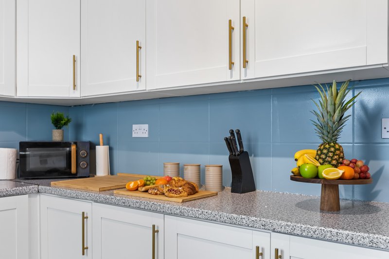 Modern kitchen with white cabinetry, blue tile backsplash, granite countertop, fresh fruit and bread displayed