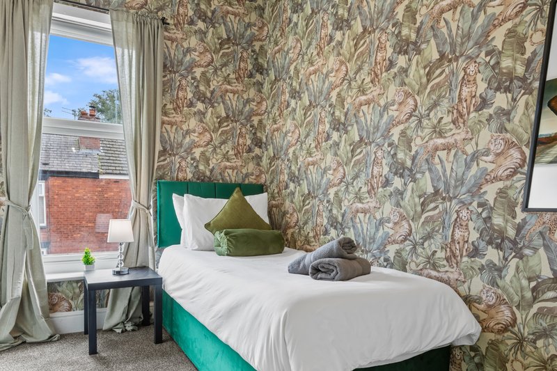 Bedroom with single bed, botanical wallpaper, window with city view, and desk