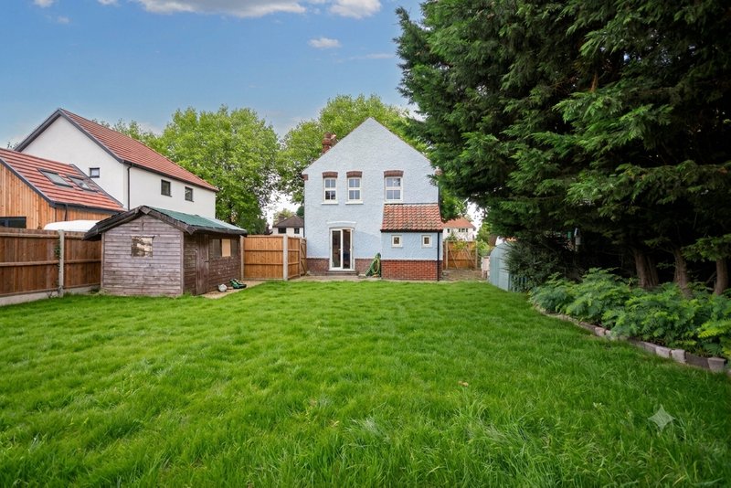 White house with garden, shed, and wooden fence surrounded by green lawn