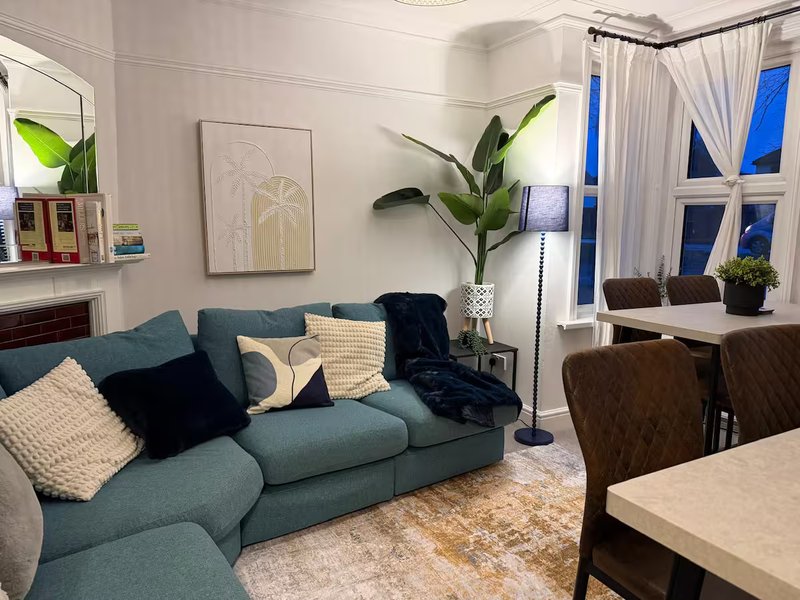 Modern living room with teal sofa, cushions, potted plants, and large windows