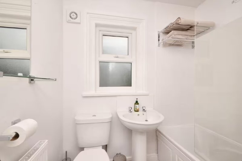 Clean white bathroom with pedestal sink, toilet, window and shower enclosure