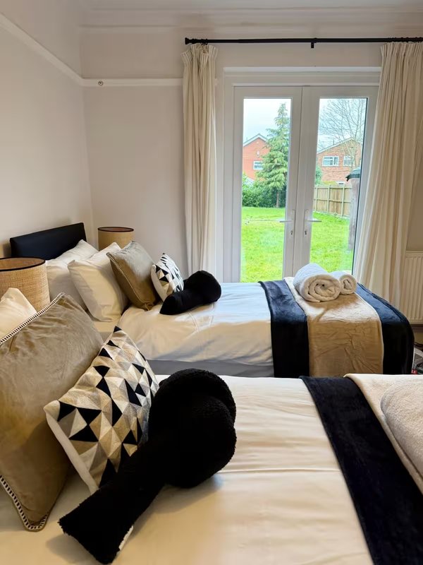 Bright bedroom with two beds, cream bedding, black cushions and throws, garden view through patio doors