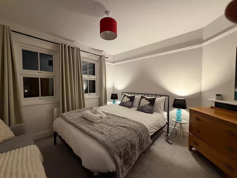 Modern bedroom with double bed, red pendant light, wooden dresser and windows with curtains