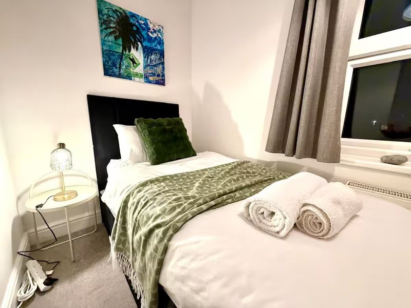 Modern bedroom with single bed, green cushion, rolled towels, bedside lamp and window