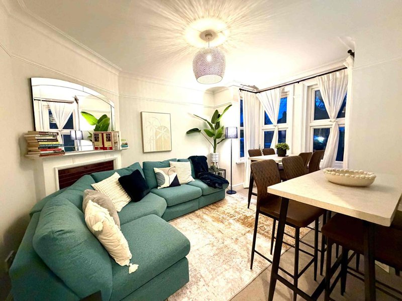 Open-plan living room with teal sofa, dining table, mirror, plants and pendant lighting
