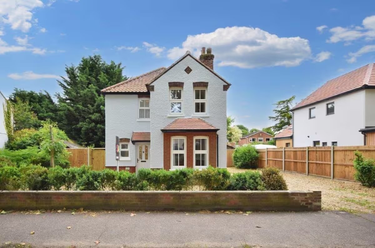 Two-storey detached house with white walls, brown brick base, front garden and wooden fence