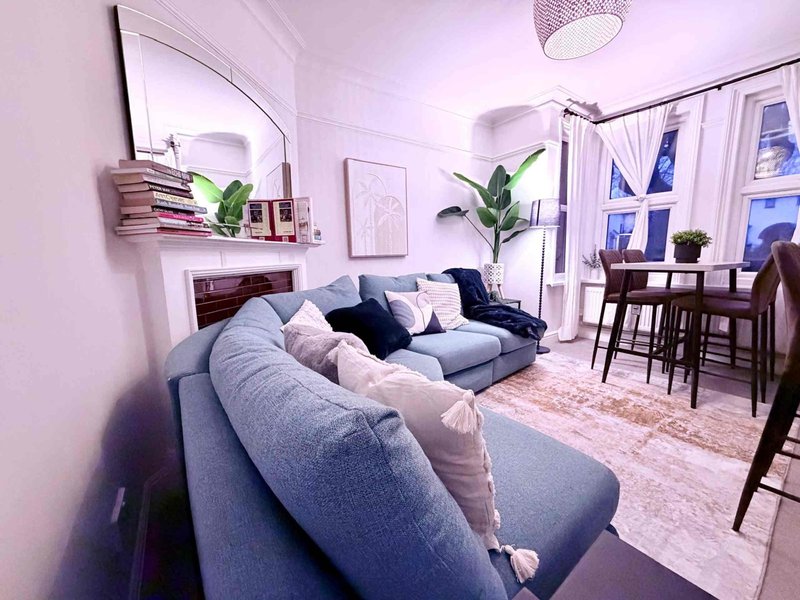 Spacious open-plan living room with grey sofa, dining table, fireplace and potted plants