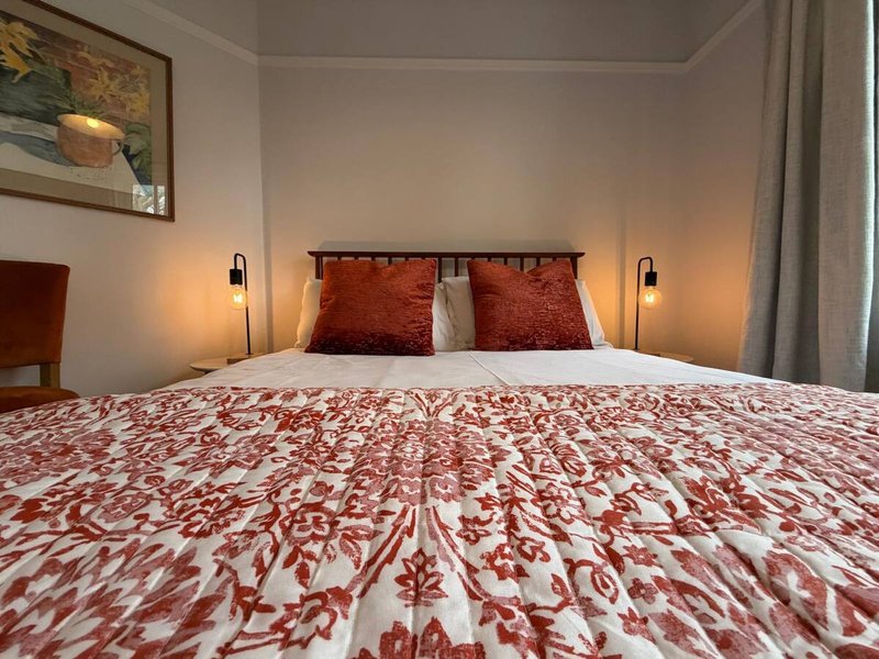 Bedroom with double bed, red patterned bedding, wall sconces, and framed artwork