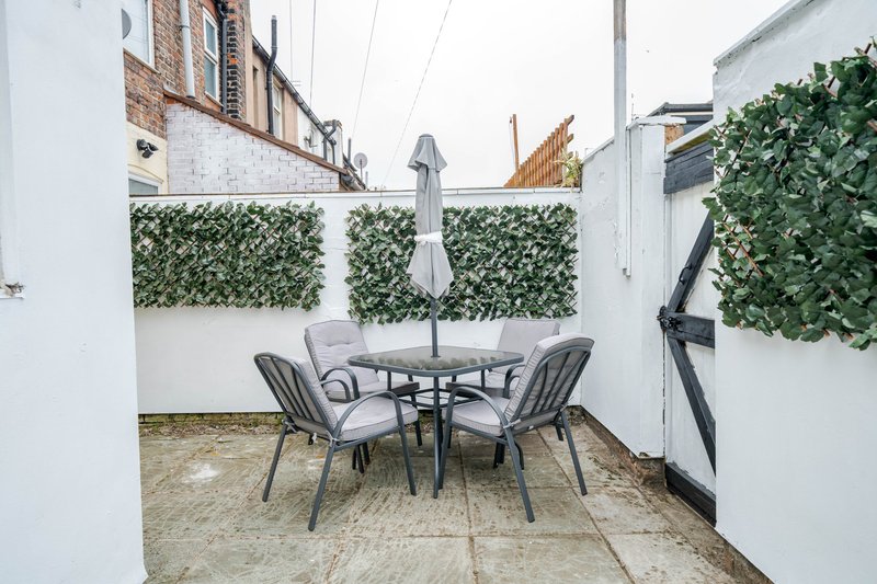 Enclosed patio area with round table, four chairs, parasol and artificial green wall panels
