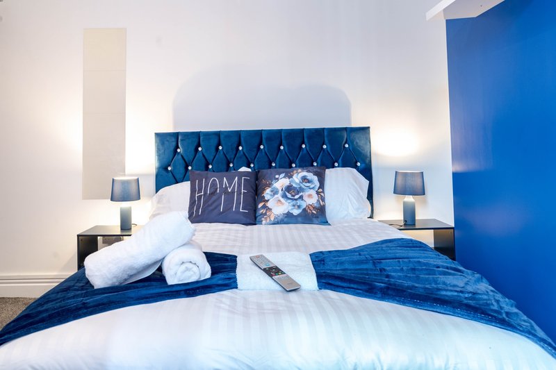 Modern bedroom with blue tufted headboard, white bedding, rolled towels, and decorative pillows