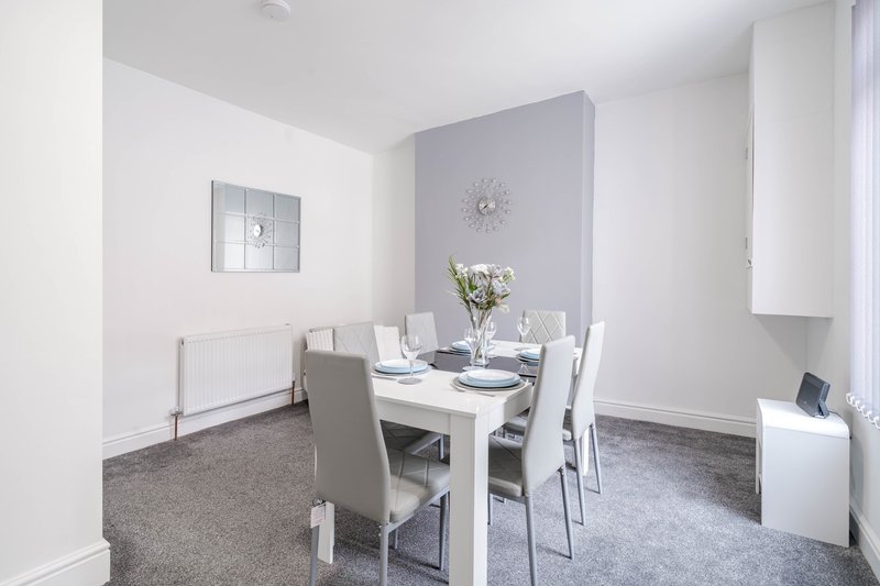Modern dining area with white table, grey chairs, grey carpet and neutral walls