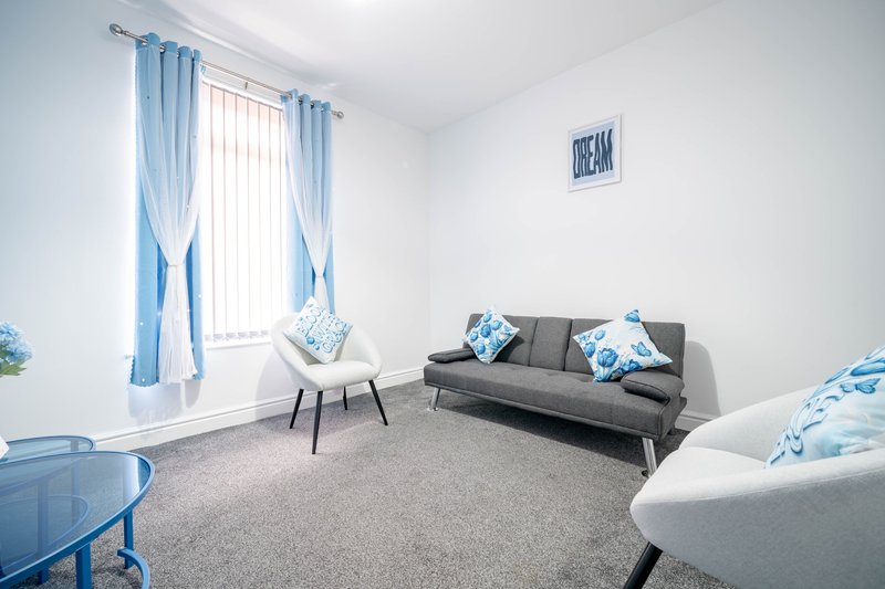 Bright living room with gray sofa, blue curtains, armchair, and window seating area