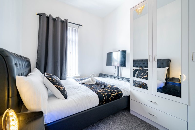Modern bedroom with double bed, white wardrobe, dark curtains and bedside lighting