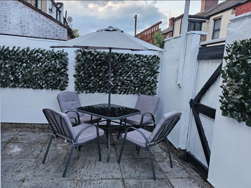 Outdoor patio with four grey chairs, black table, and grey umbrella against white walls