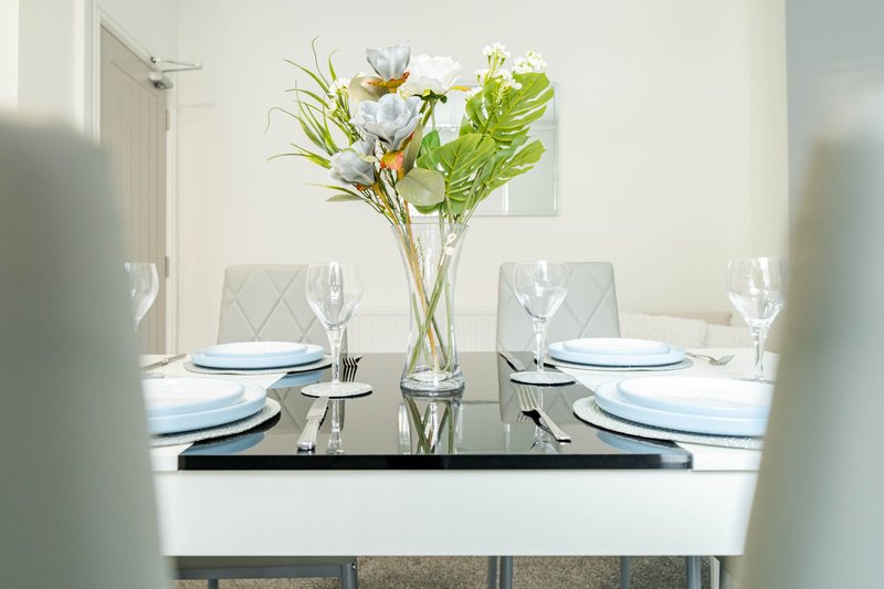 Dining table set for four with white plates, glasses, and fresh flower arrangement