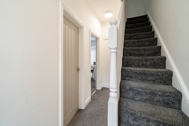 Hallway with staircase, white walls, closed doors, and carpet flooring