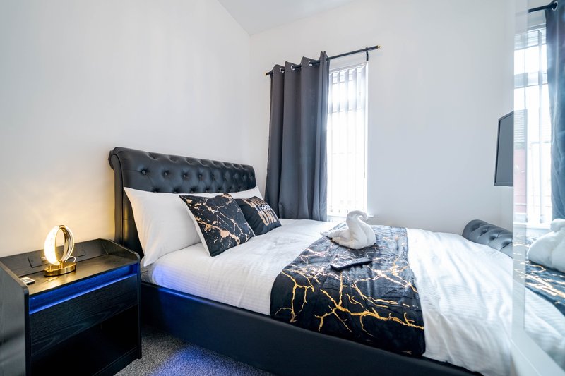Modern bedroom with upholstered black headboard, double bed, gold patterned bedding, and bedside lamp