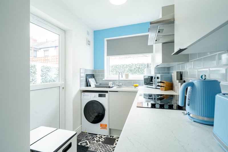 Modern kitchen with blue accent wall, washing machine, white countertops and appliances