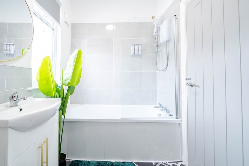 Clean modern bathroom with white tiles, bath tub, sink and bright yellow flowers in vase