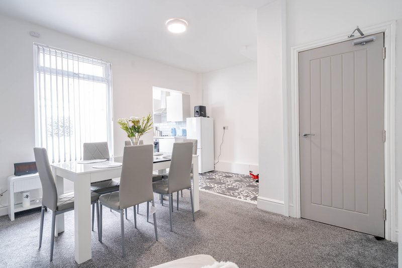 Modern dining area with white table, grey chairs, and desk workspace by window
