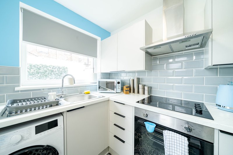 Modern kitchen with white cabinetry, stainless steel appliances, blue accent wall and subway tile backsplash