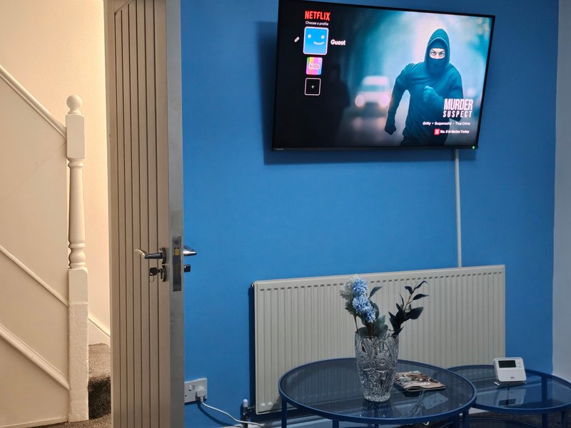 Blue bedroom with wall-mounted TV, radiator, round black table with vase, and white door