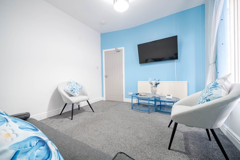 Bright modern bedroom with blue accent wall, TV, two armchairs, and seating area